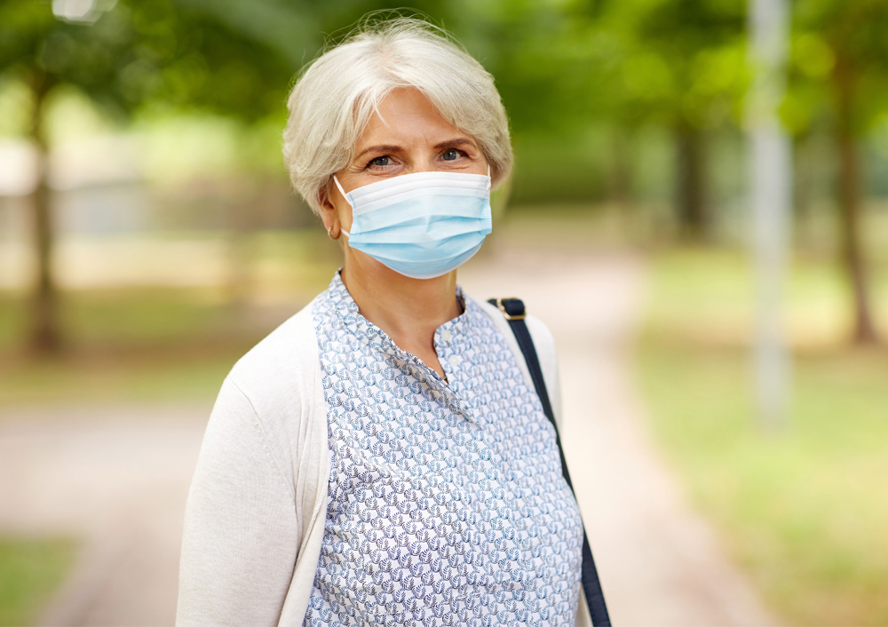 A woman wearing a mask while standing on the sidewalk.